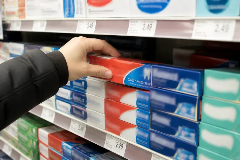 Hand selecting a cavity-protection fluoride toothpaste box on a store shelf